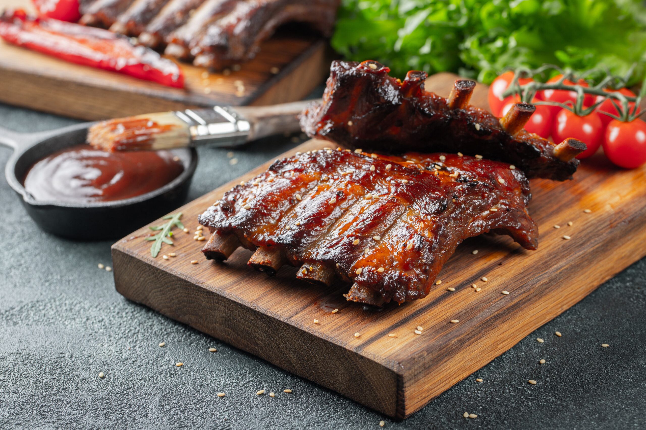 Closeup of pork ribs grilled with BBQ sauce and caramelized in honey. Tasty snack to beer on a wooden Board for filing on dark concrete background.