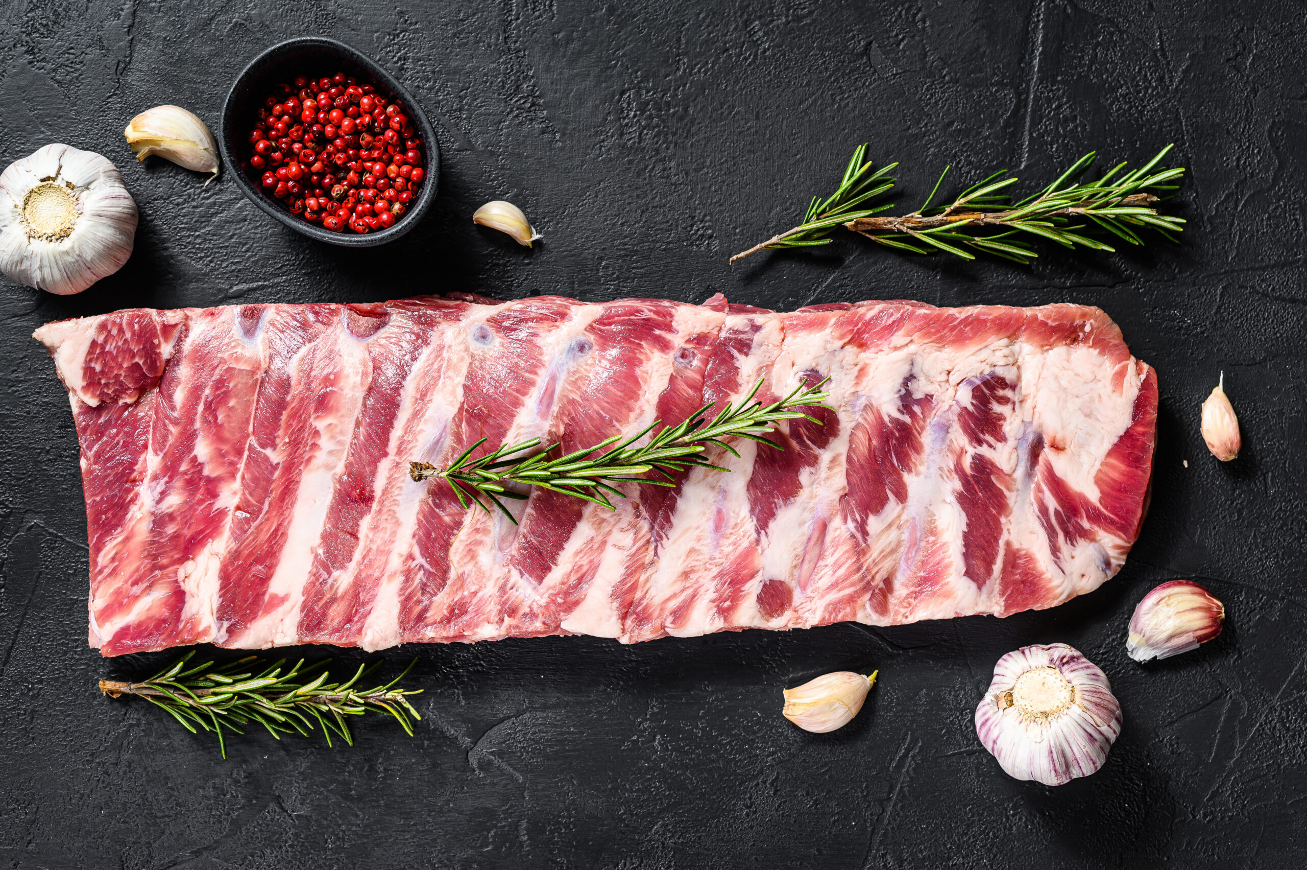 rack of raw pork spare ribs seasoned with spices. Black background. Top view.